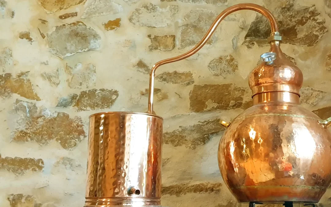 Cuve et alambic en cuivre pour gin, connectés par un distillateur, contre un mur en pierre.