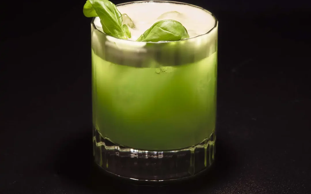 Verre à gin vert pastel, garniture de feuilles de basilic, sur fond sombre, mettant en valeur une boisson artisanale rafraîchissante.