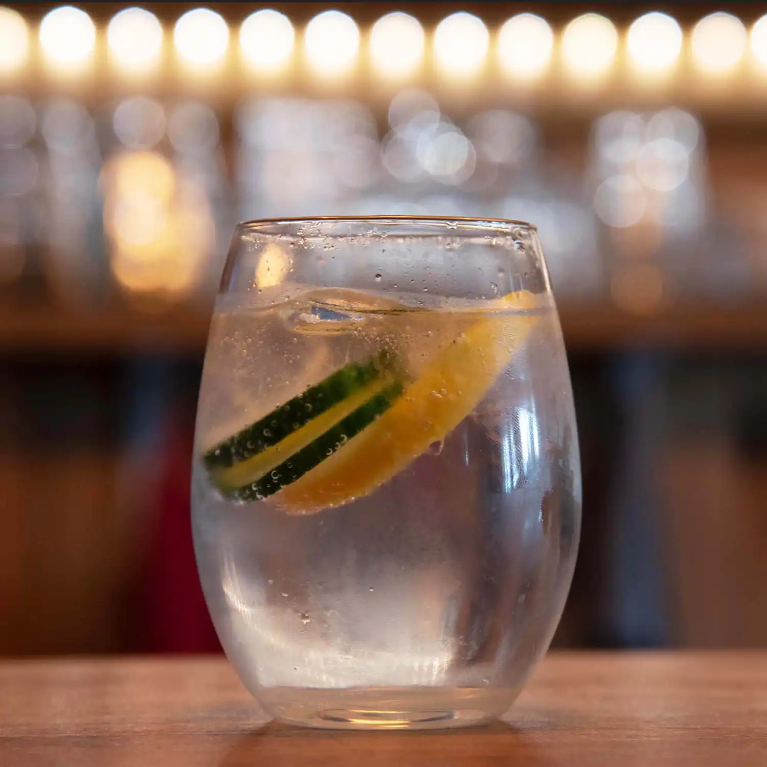 Verre cocktail gin été rafraîchissant avec tranches de citron vert et citron, glaçons et liquide clair sur plan de bar.